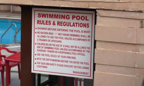 Sign saying 'swimming pool rules & regulations' in bold red text on white background.