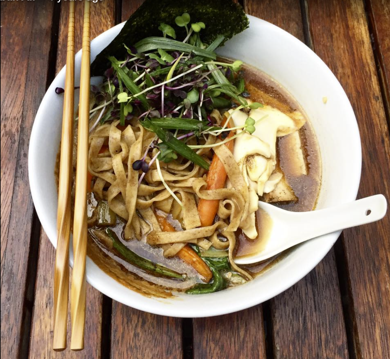 An appetizing image of uneaten soup with a spoon and chopsticks on a clean table